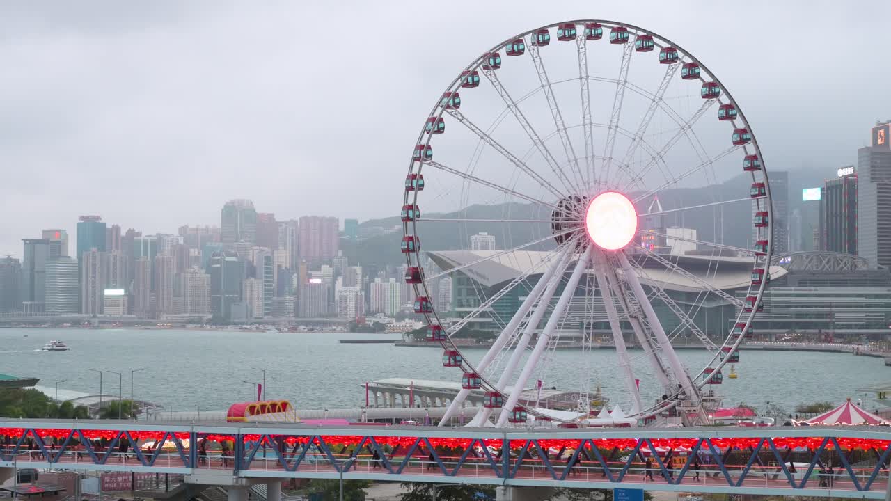 un puente peatonal está decorado con faroles rojos chinos mientras la gente camina a través de él mientras, en el fondo, hay una rueda de la fortuna en hong kong