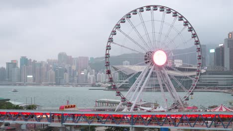 a pedestrian bridge is decorated with chinese red lanterns as people walk through it while, in the background, there is a ferris wheel in hong kong