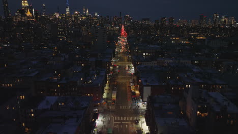 Backwards-fly-above-long-straight-street-in-city.-Revealing-skyline-with-famous-high-rise-downtown-buildings.-Night-city-scene.-Manhattan,-New-York-City,-USA