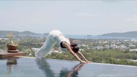 adult woman doing balancing exercise poolside against amazing landscape of resort on sea shore