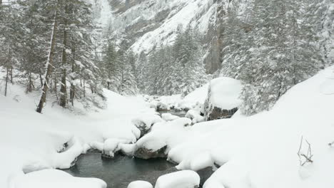 Moving-low-over-calm-creek-in-snow-covered-landscape