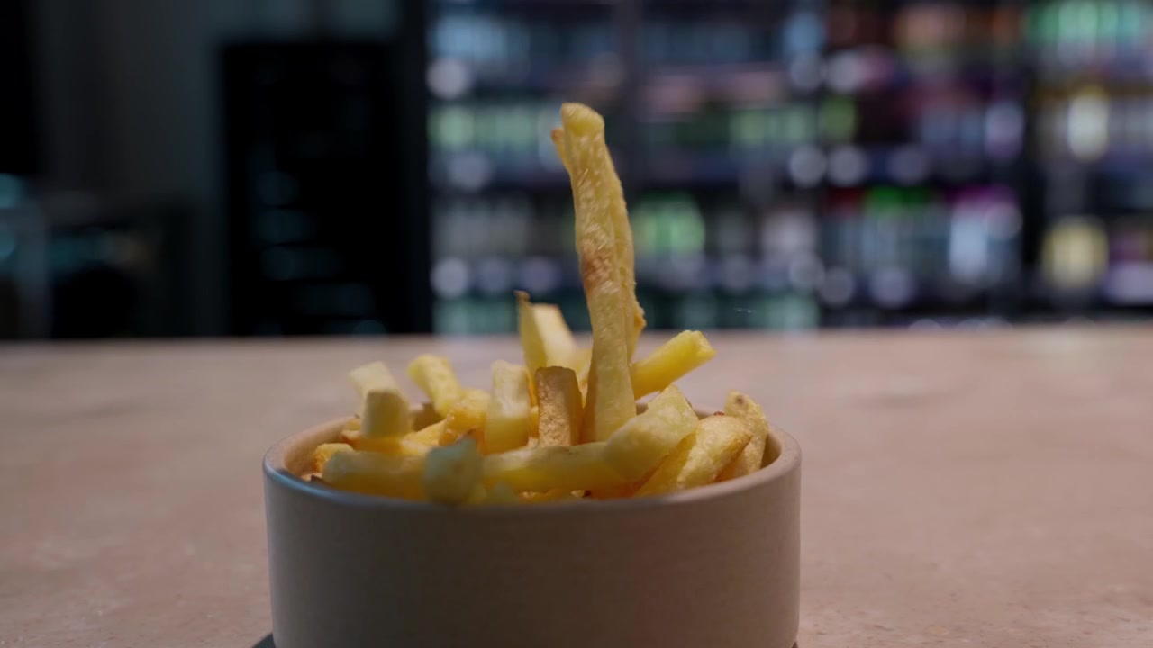 French fries dropping into a bowl in a commercial kitchen or food service setting. Useful for fast food, catering, restaurant and snack themes, slow motion close-up