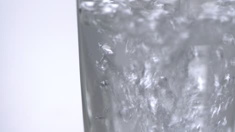 verter agua mineral fresca en un vaso en una mesa. bebida espumosa fresca con bolas de oxígeno en fondo blanco