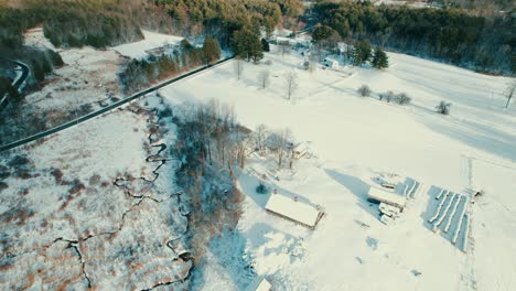 Tilting-up-angle-of-top-down-snow-covered-fields-up-to-overlooking-a-scenic-winter-landscape-with-winding-creeks,-rolling-hills,-and-evergreen-forests