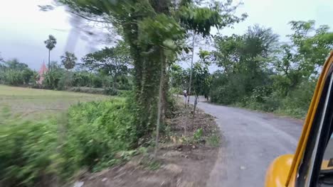 POV-shot-of-a-Bengal-Yellow-Taxi-travelling-through-village-mud-roads-with-trees-on-both-sides