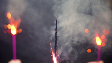 sparkler center foreground and two background defocused giving off sparks and light with colorful bokeh background