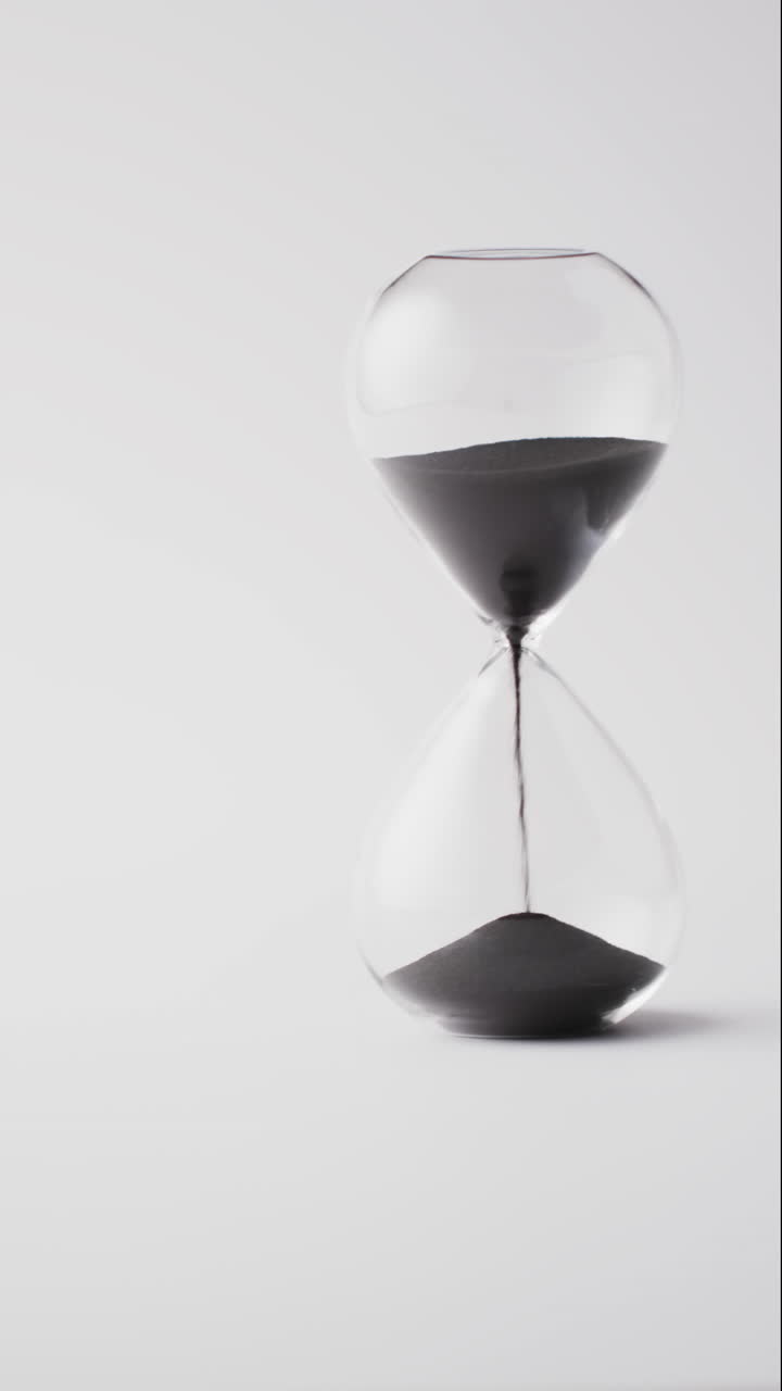 Vertical video of hourglass with sand pouring, copy space on white background