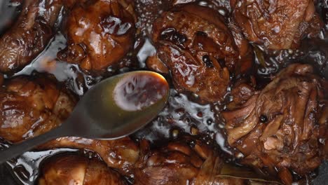 pouring dark adobo sauce over braising chicken thighs and chicken legs with a spoon