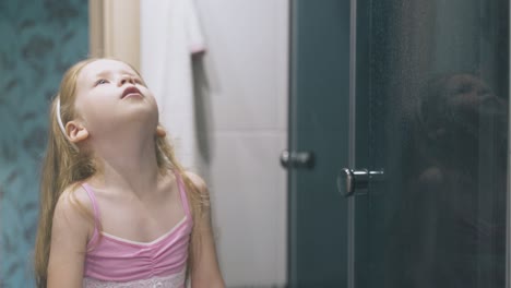 cute girl in pink shirt gargles sore throat at large mirror