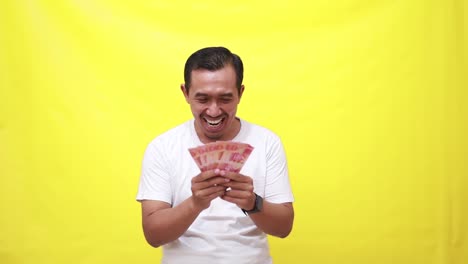 happy asian adult man holding indonesia banknotes while touching his chest