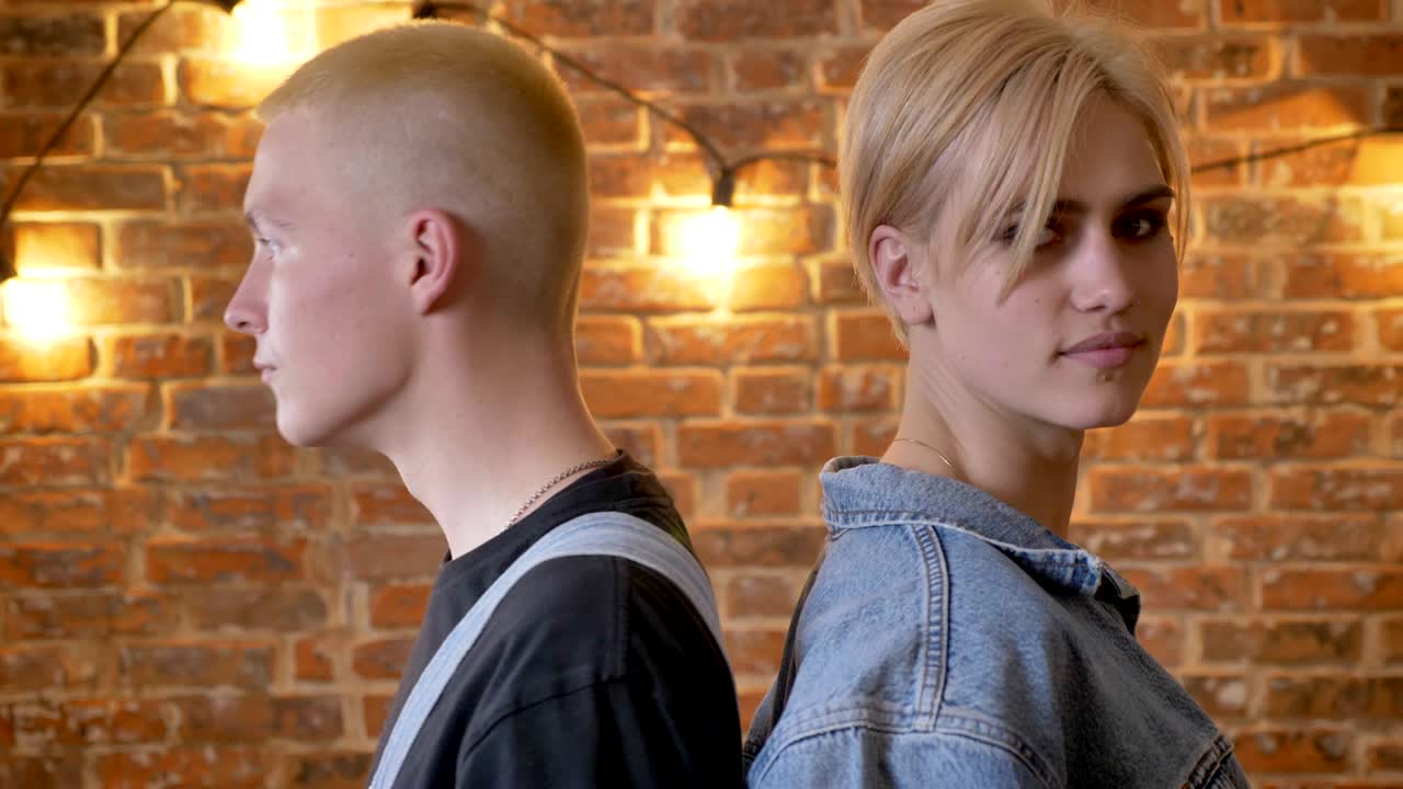 una joven pareja de hipsters está de pie espalda a espalda, bailando, moviendo el cuello, moviéndose concepción, fondo de ladrillo, primer plano