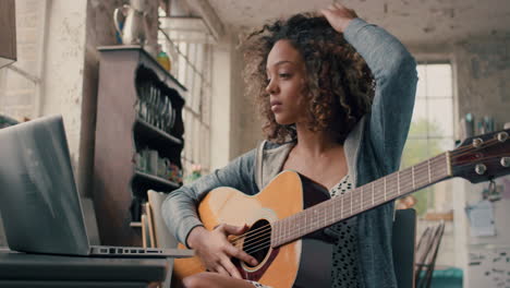 chica joven de raza mixta atractiva aprendiendo a tocar la guitarra usando una computadora portátil