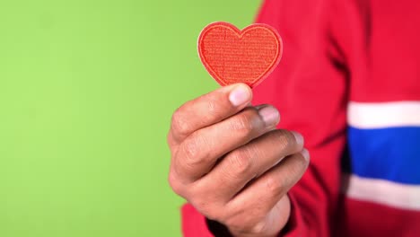 hombre con una mano que sostiene un corazón rojo sobre un fondo verde