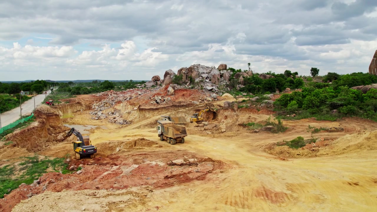 Veduta aerea di un cantiere edile con escavatori, camion, alberi, una grande collina e nuvole nel cielo a Telangana, India. Di giorno, zoom in, ripresa con drone, 4k.