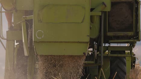 Rear of a green combine harvester releasing straw in slow motion, detail zoom