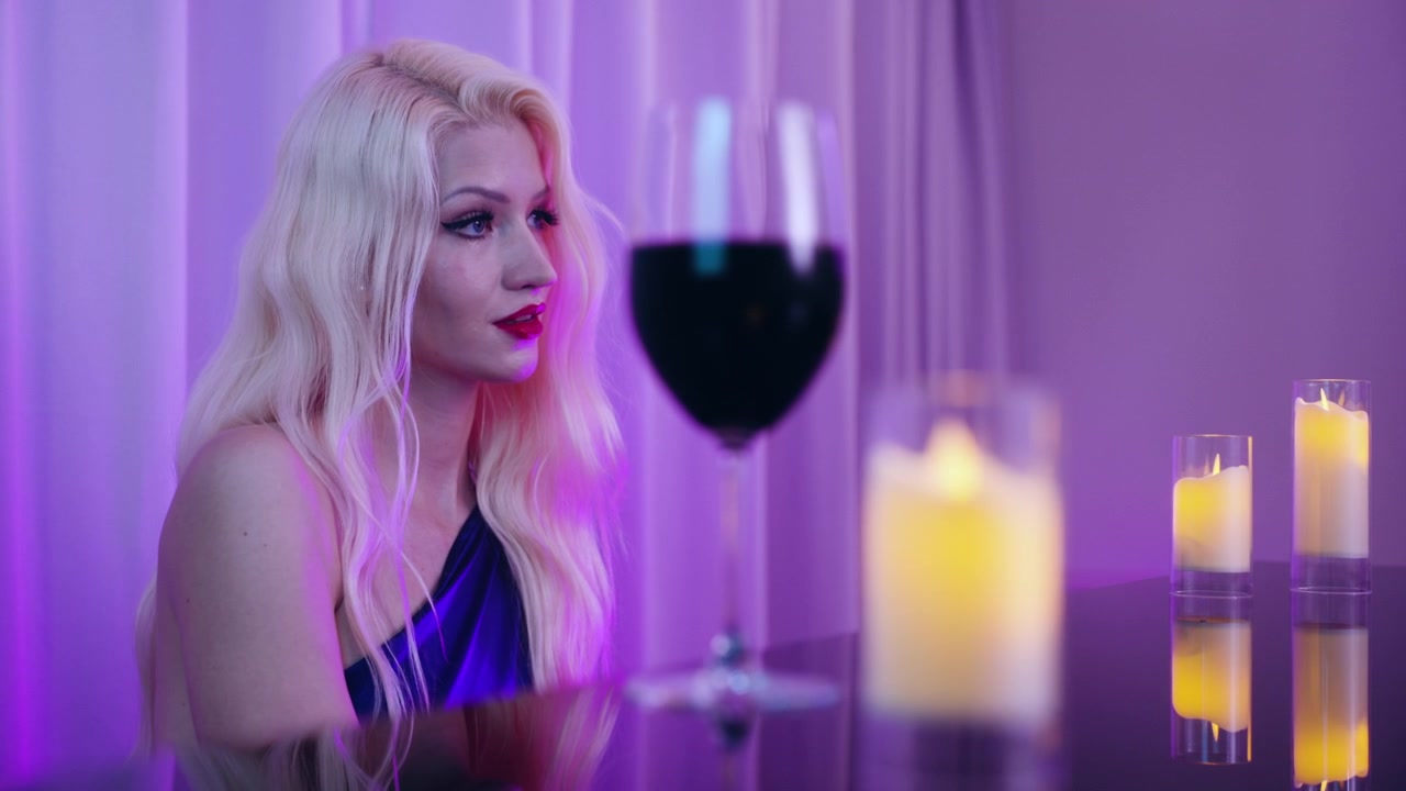 Donna bionda attraente e graziosa che suona il pianoforte a casa, illuminata da luce viola e candele.