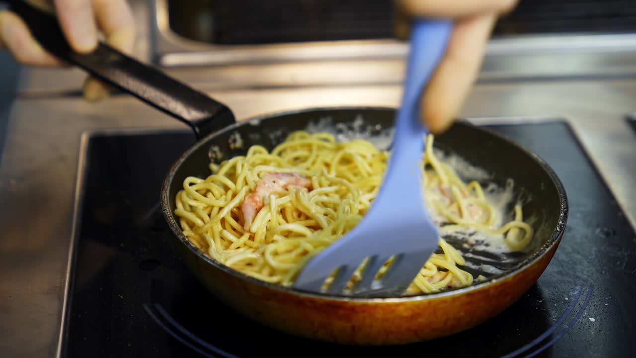 Man`s hands with kitchen spatula mixes pasta with sauce in frying pan. Selective focus. Tasty dinner.