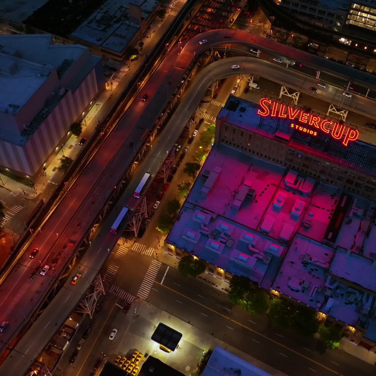 Silvercup Studios surrounded by roads with lively traffic at night time. Top view on the roofs of buildings with gradual descending