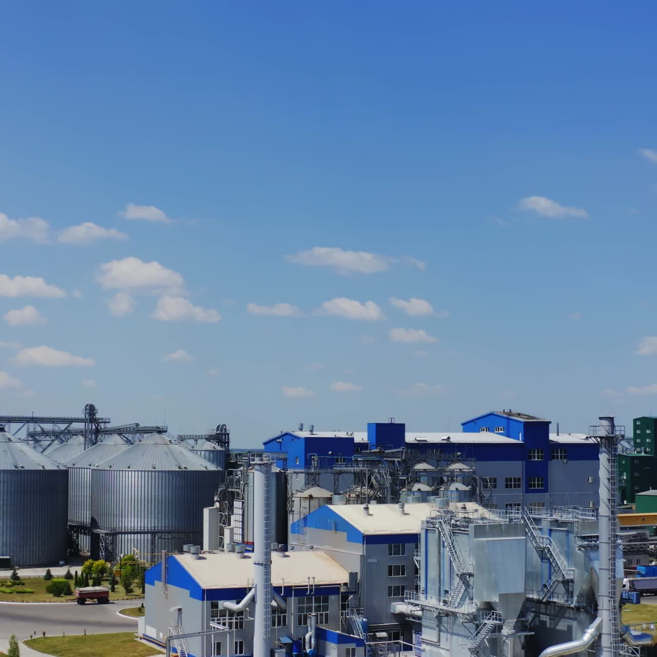 Innovative plant for grain processing. Modern building and elevators for grain on field under blue sky. Agribusiness concept.