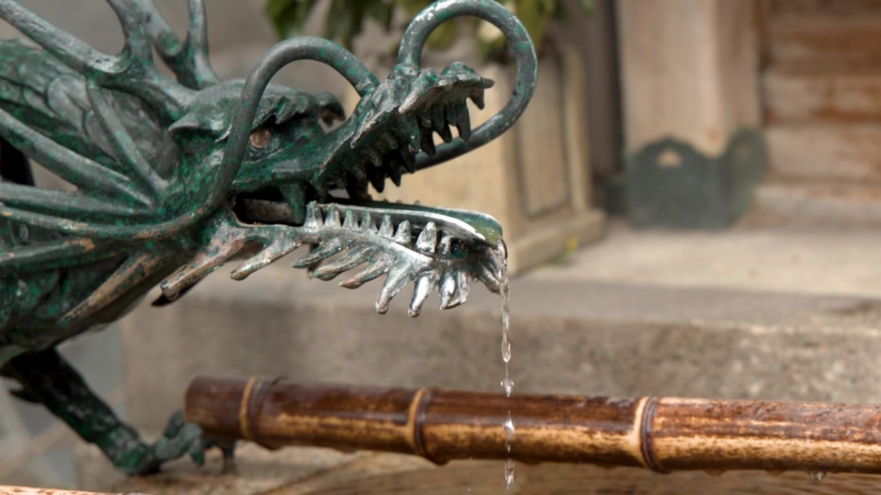 Primo piano di acqua che gocciola da una statua di drago in bronzo in una fontana di purificazione in bambù.