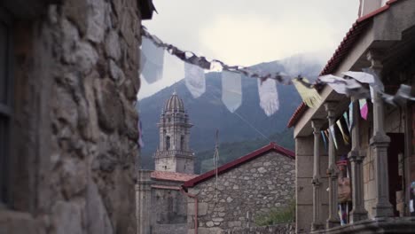 Feiern-Von-Fahnen,-Die-Am-Jakobsweg-Hängen,-Mit-Dem-Glockenturm-Des-Klosters-Von-Oia-Im-Hintergrund-In-Zeitlupe-Und-Weichem-Fokus