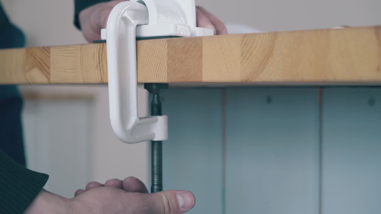 man puts fixing detail to four mill on table in kitchen