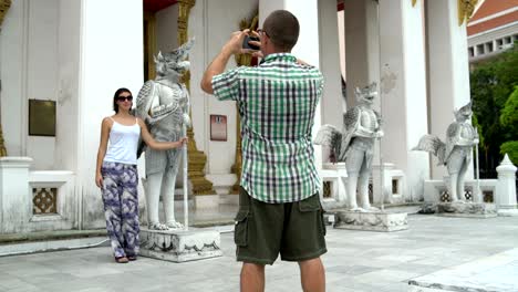 a man is taking pictures of a woman next to a mythological statue on a smartphone