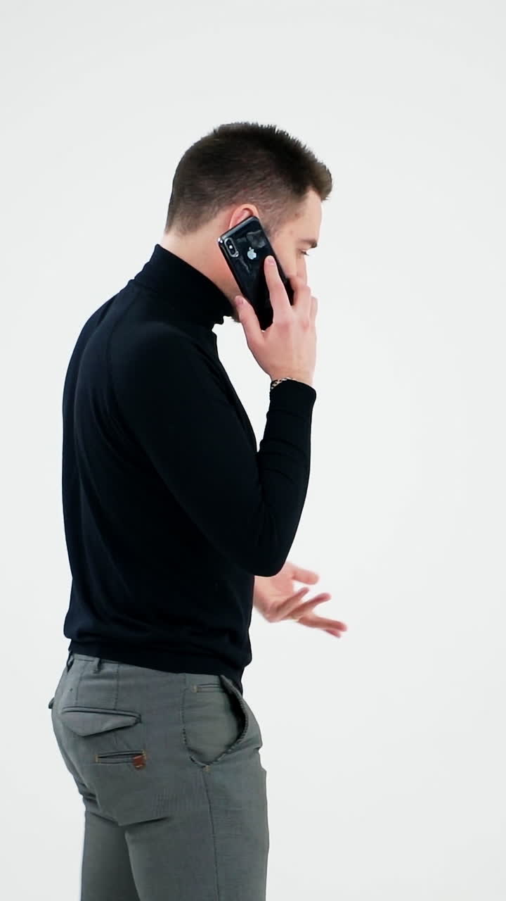 Handsome man having phone talk indoors. Serious young businessman talking on a cellphone and moves slowly isolated on white background. Slow motion. Vertical video