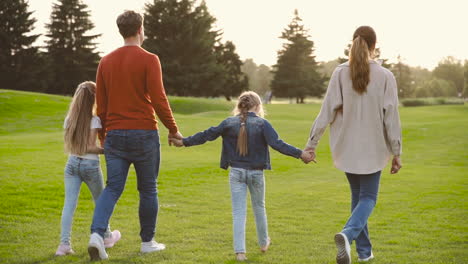 widok z tyłu szczęśliwej rodziny trzymającej się za ręce i biegającej razem w parku