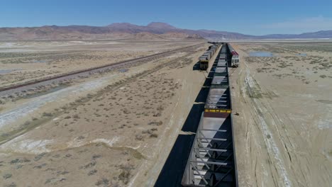 high overhead, forward motion aerial view of empty train cars on three merging tracks in the desert