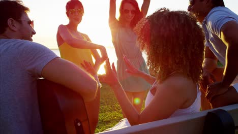 amigos multiétnicos tocando la guitarra en la playa del atardecer