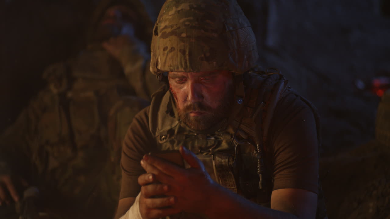 Injured soldier using a smartphone at night near a campfire.