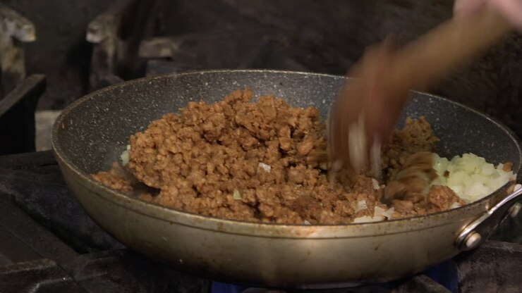Aggiunta di macinato vegetariano a cipolle che sobbollono su fiamma a gas