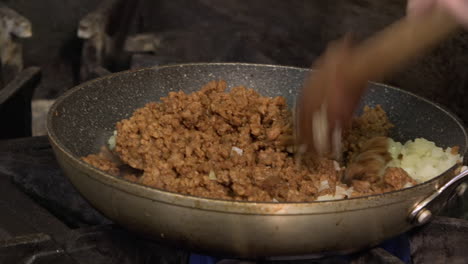 adding vegetarian ground beef to simmering onions over a gas flame