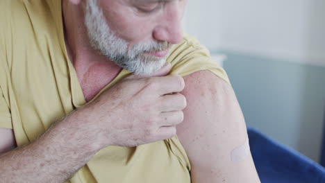 happy caucasian mature man showing plaster on arm where he was vaccinated against coronavirus