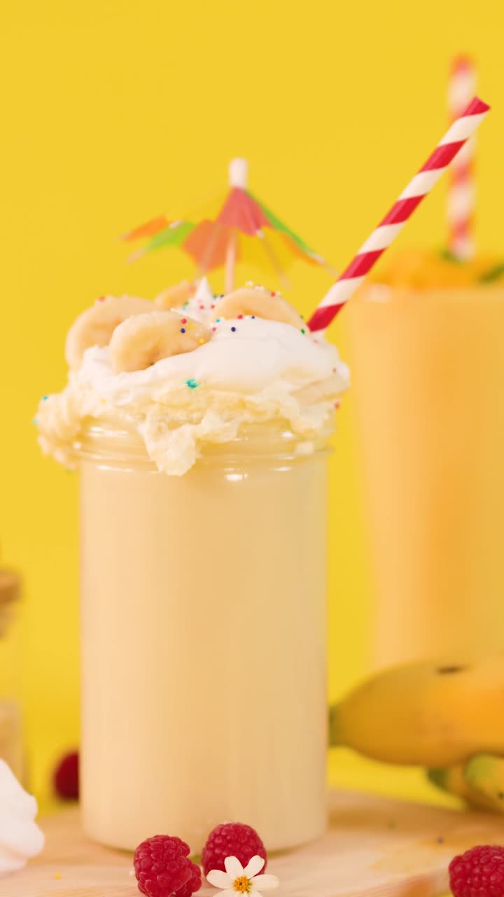 Primo piano verticale di un cremoso milkshake alla banana guarnito con panna montata e frutti di bosco freschi.