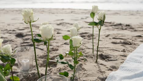 close up of white roses and glass candles arranged on sandy beach for serene ceremony
