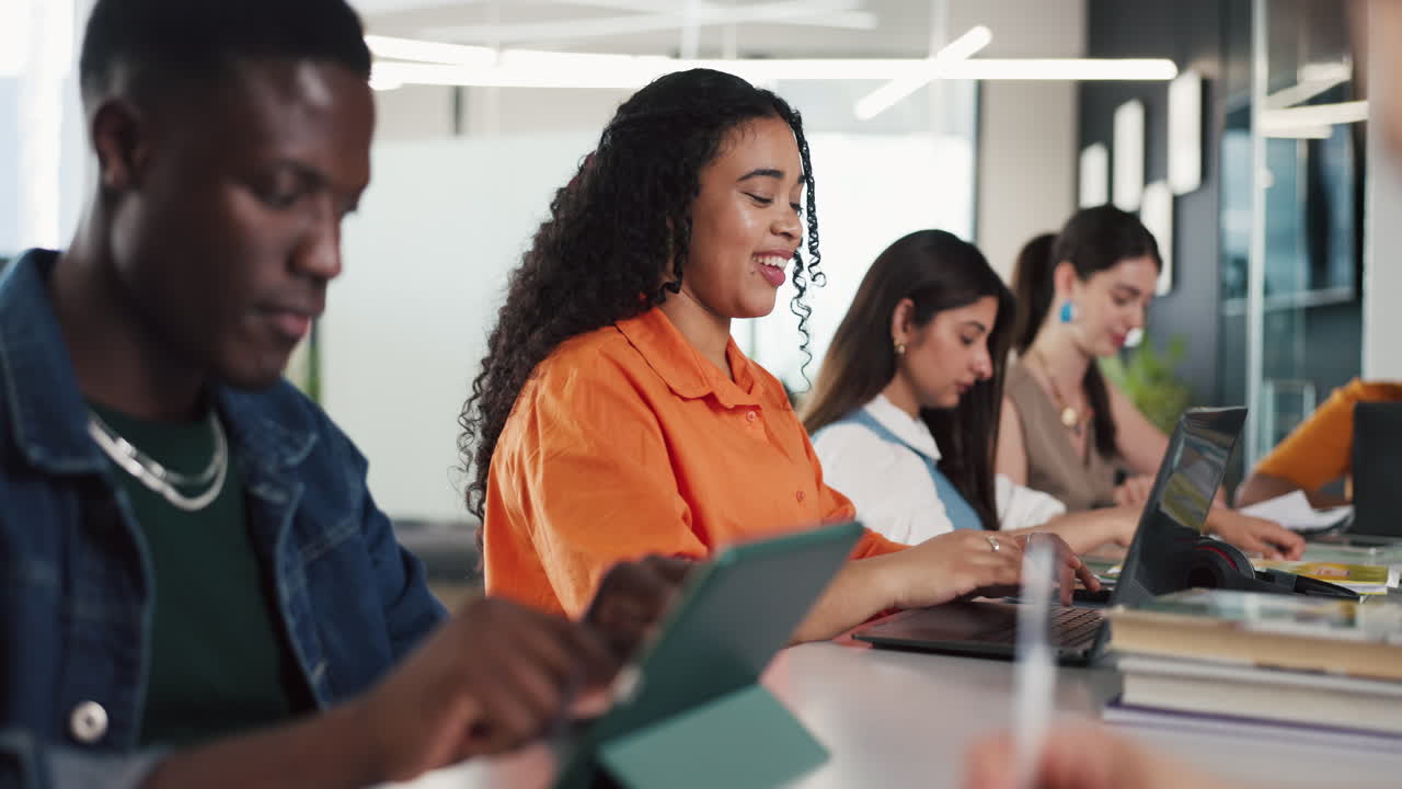 Gruppo eterogeneo di studenti che lavorano su laptop e tablet in un'aula moderna.