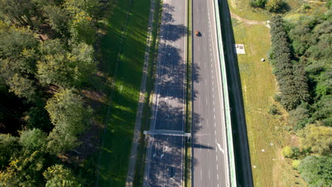 Aerial-view-of-a-highway-with-adjacent-lush-greenery,-casting-long-shadows-from-tall-trees