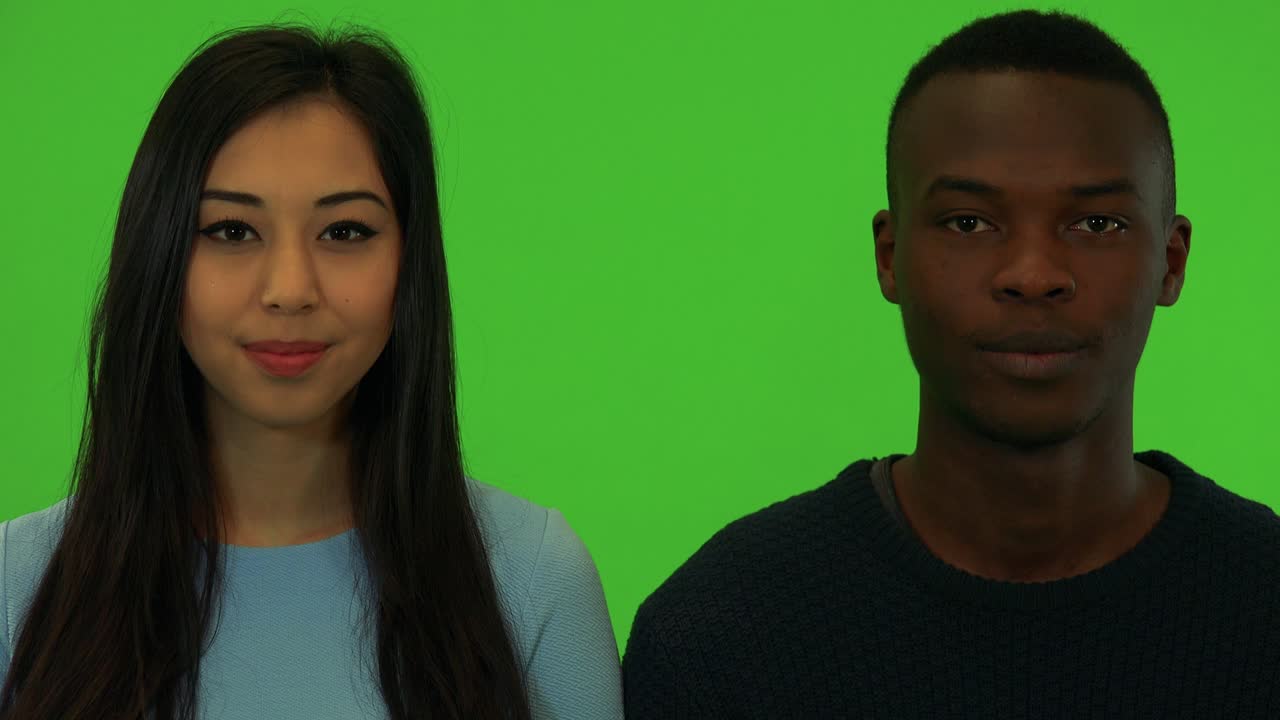 Una joven asiática y un joven afroamericano sonríen a la cámara - primer plano de los rostros - estudio con pantalla verde