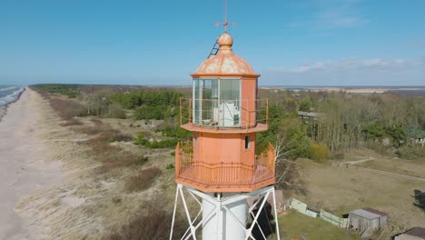 Aerial-establishing-view-of-white-colored-Pape-lighthouse,-Baltic-sea-coastline,-Latvia,-white-sand-beach,-large-waves-crashing,-sunny-day-with-clouds,-orbiting-drone-shot