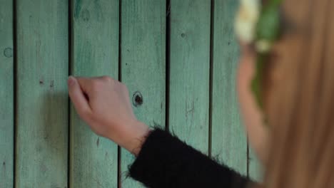 Brunette-female-knocking-on-old-green-rural-wooden-doors,-back-view