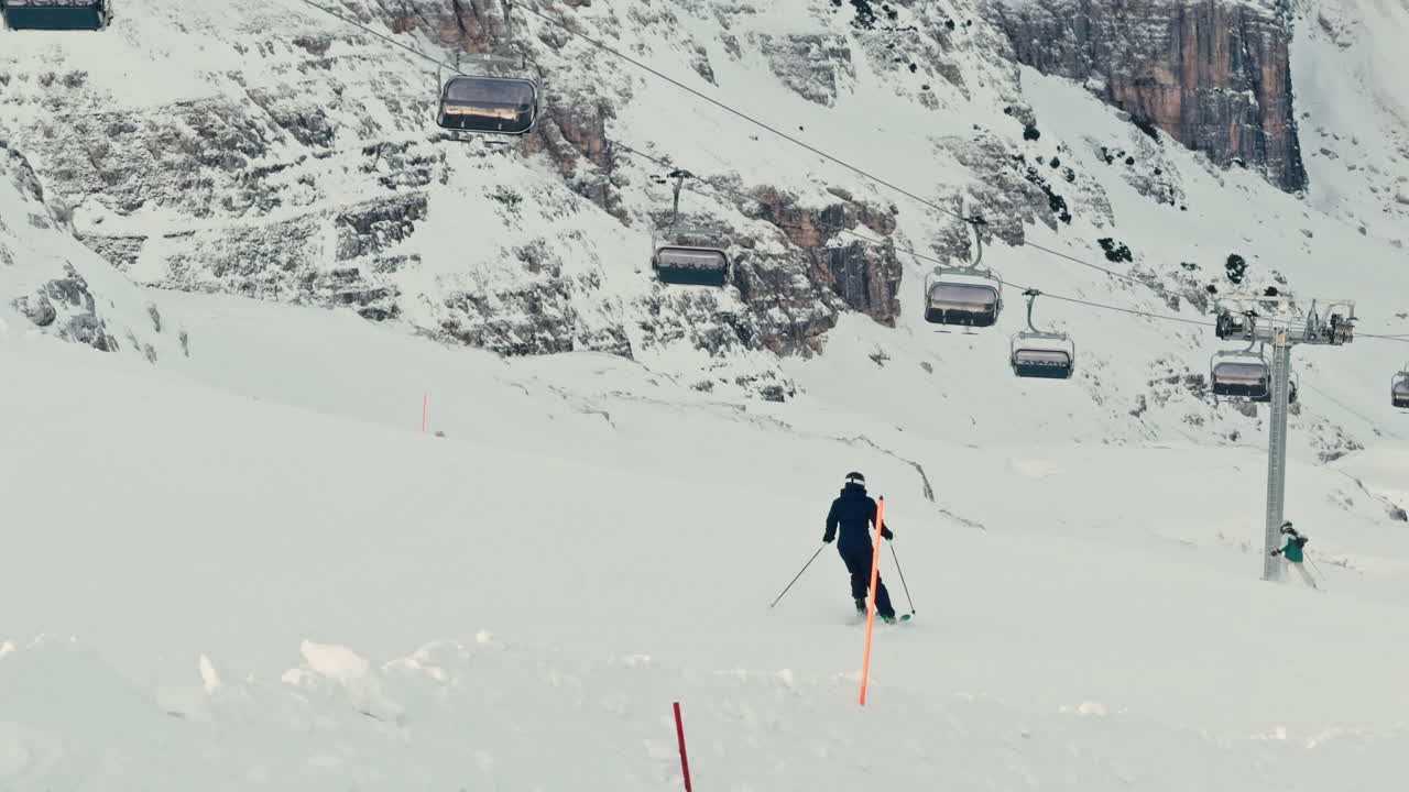 Slow pan across winter mountains in the Dolomites with skiers skiing with alpine terrain