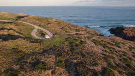 Cinematic-aerial-orbital-shot-around-a-camper-van-camping-by-the-Atlantic-Ocean-at-Praia-da-Bordeira-on-the-Algarve-coast-in-Portugal-at-sunrise