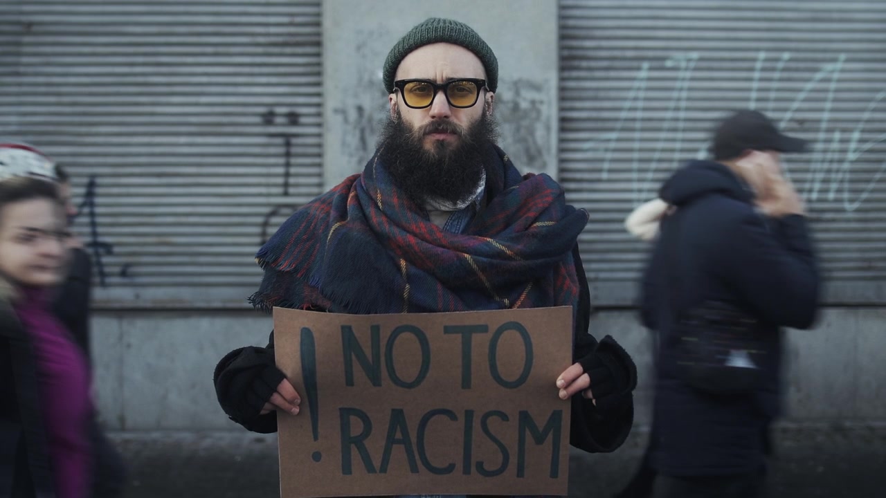 Man Holding No To Racism Sign on Busy City Street