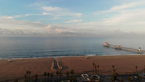 4k-ariel-drone-pan-of-the-stunning-horizon,-beach,-pier,-and-surfers-surfing-as-families-vacation-in-Surf-City-USA,-Southern-California,-Huntington-Beach