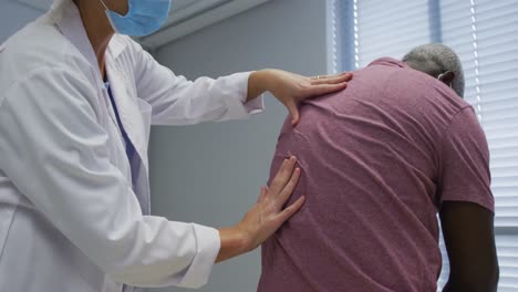 Diverse-female-orthopedic-doctor-examining-male-patient-in-face-masks