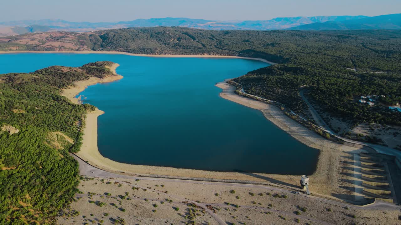Stunning aerial view of a serene reservoir nestled in the Tunisian landscape. Crystal clear waters meet lush green hills.