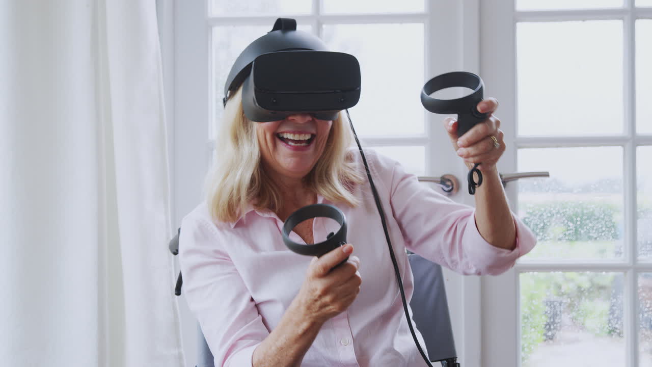 Donna matura disabile su sedia a rotelle a casa che usa un visore per la realtà virtuale giocando e tenendo i controller.