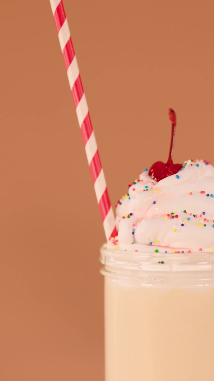 Una mano inserisce una cannuccia a strisce rosse e bianche in un milkshake con panna montata